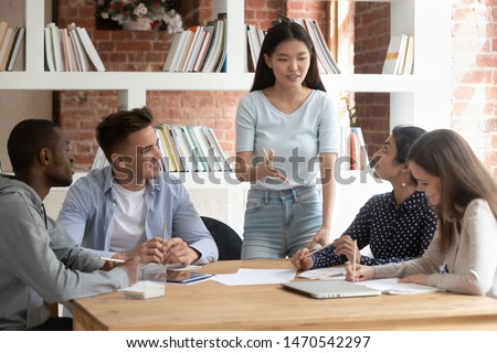 Smiling motivated asian female team leader holding meeting with diverse groupmates, explaining new project detail. African american, indian and caucasian concentrated students discussing assignment. Royalty-Free Stock Photo #1470542297
