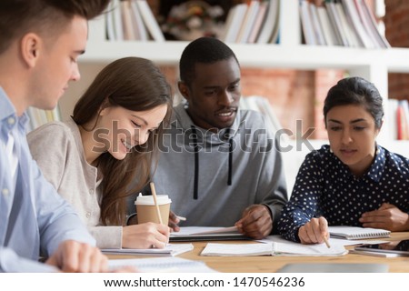Smiling group of diverse students preparing for seminar or session together. Indian female teammate explaining home task for african american concentrated guy. Positive college friends doing homework. Royalty-Free Stock Photo #1470546236