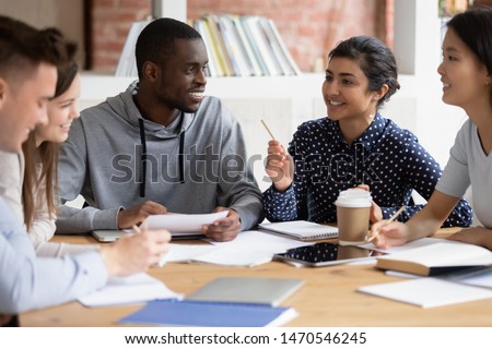Happy diverse college friends listening to indian female teammate, explaining home task. Mixed race group of students discussing new school project ideas together, preparing for session at classroom. Royalty-Free Stock Photo #1470546245