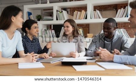 Group of happy diverse students sitting together at shared table in library, discussing school project together. Mixed race college friends preparing for exams or tests, collaborating in classroom. Royalty-Free Stock Photo #1470546314