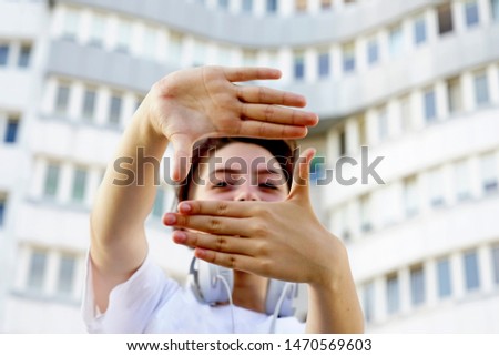 Portrait of playful beautiful caucasian woman pretending to take photo with her hands while walking on the street. Attractive model posing, using hands to make a frame outdoors in summer