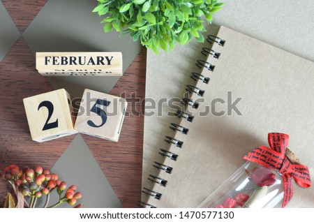 February 25. Date of February month. Number Cube with a flower, Rose bottle and notebook on Diamond wood table for the background.