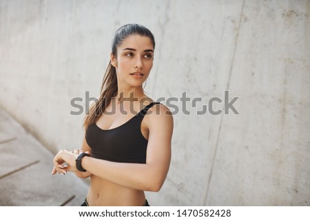 Checking vitals before running marathon. Motivated good-looking sporty woman in sports bra use fitness tracker to measure heart rate, look aside how many laps left during morning jogging session Royalty-Free Stock Photo #1470582428