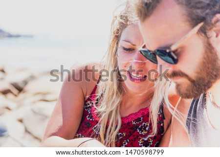A couple in a relationship having a good time outdoors with a smartphone in summer holidays in the beach