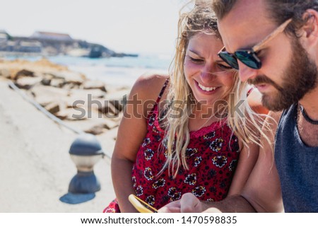 A couple in a relationship having a good time outdoors with a smartphone in summer holidays in the beach