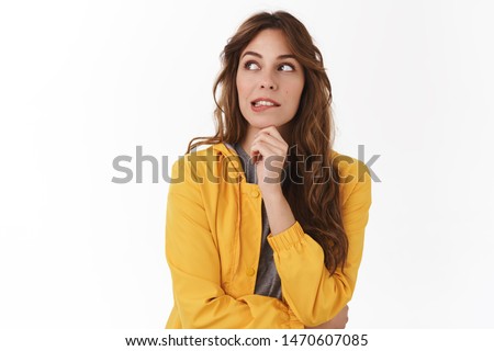 Yikes shall I. Doubtful pretty caucasian curly-haired young woman yellow jacket smirking look away hesitant pondering tough decision touch chin thoughtful unsure how act standing white background Royalty-Free Stock Photo #1470607085