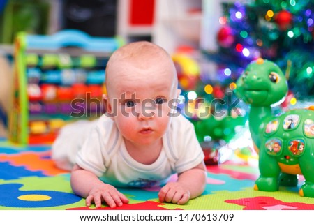 cute baby boy laying under che Christmas tree with his dinosaur