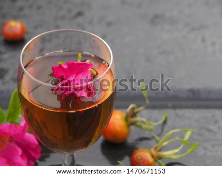 Wine in a transparent glass of a healthy drink and rosebud. Goblet with a beautiful tincture, rose flower and berries on a wet table in the rain. Original picture for the wishes of good health.