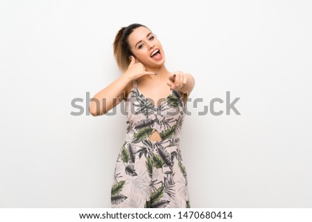 Young woman over isolated white background making phone gesture and pointing front