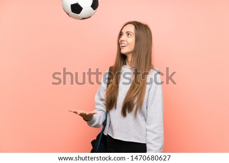 Happy Young sport woman over isolated pink background holding a soccer ball