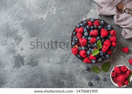 Fresh raspberries and blueberries in plate on dark background. Copy space