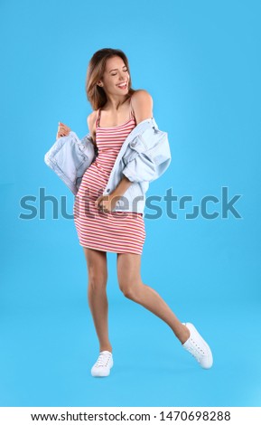 Beautiful young woman in dress and jacket dancing on blue background