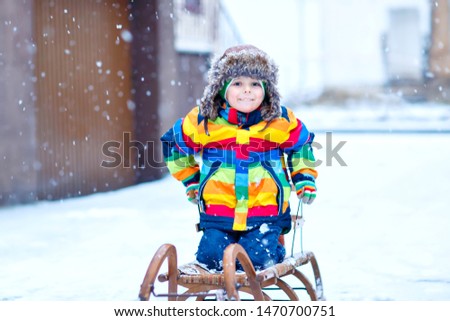 Little kid boy enjoying sleigh ride during snowfall. Happy preschool kid riding on vintage sledge. Child play outdoors with snow. Active fun for family Christmas vacation in winter