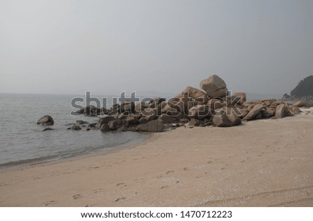 A picture of tranquil summer beach with rocks on a slightly hazy day.