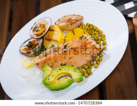 Picture of  tasty fried trout  fillets, served at plate with dog cockle, avocado and vegetables