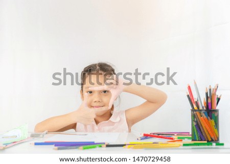 Little girl shows a frame from hands like photo, Kid drawing with colorful pencils