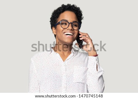 Head shot excited happy smiling african american young woman in eyeglasses talking on cellphone with friend, listening to good news, business success or win notice, isolated on grey studio background. Royalty-Free Stock Photo #1470745148