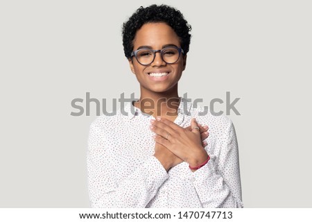Sincere thankful smiling african american woman holding hands near heart on chest, looking at camera. Head shot close up portrait grateful woman in eyeglasses, isolated on grey studio background. Royalty-Free Stock Photo #1470747713