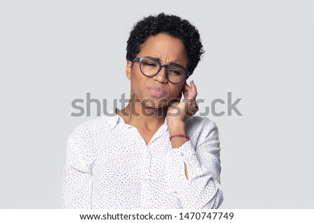Sick irritated african american young woman suffering from strong earache head shot. Unhealthy ill ethnic frowning woman in glasses touching ear, tired of noise, isolated on gray studio background. Royalty-Free Stock Photo #1470747749