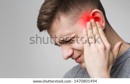 Young man has sore ear, suffering from otitis, touching his inflamed head, close up, empty space Royalty-Free Stock Photo #1470801494