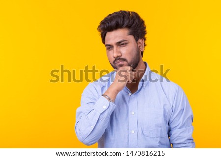 Apathetic cute young indian man is posing on a yellow background with copy space and thinking about something. Concept of unfulfilled dreams.