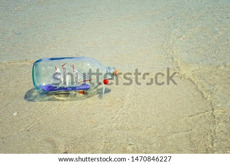 Glass bottle with a boat on the beach on the background of the sea