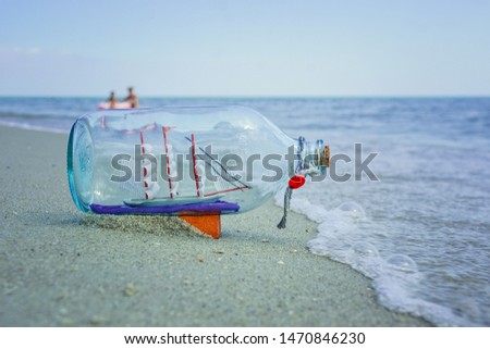 Glass bottle with a boat on the beach on the background of the sea