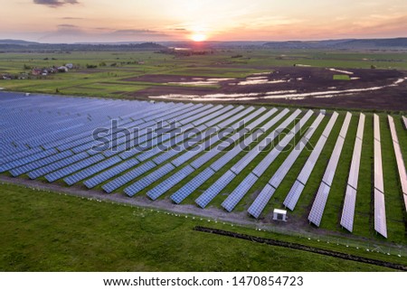 Blue solar photo voltaic panels system producing renewable clean energy on rural landscape and setting sun background. Royalty-Free Stock Photo #1470854723