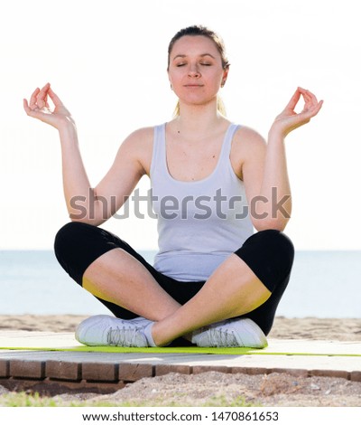 Young woman doing yoga poses cross-legged on beach at daytime