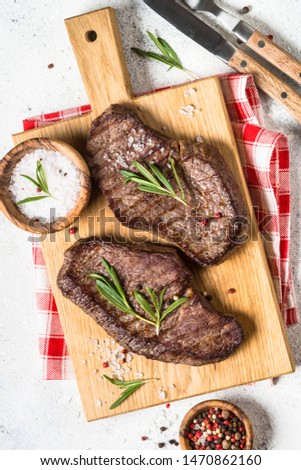 Grilled beef steak on wooden cutting board on white background. Top view.