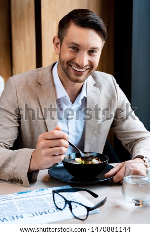 smiling businessman looking at camera while eating in cafe