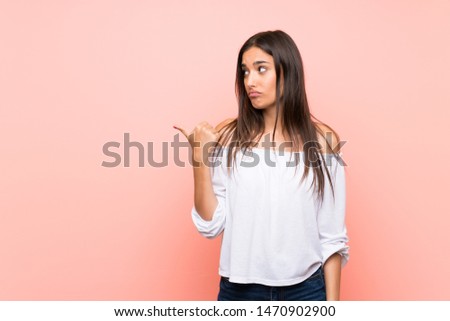 Young woman over isolated pink background unhappy and pointing to the side
