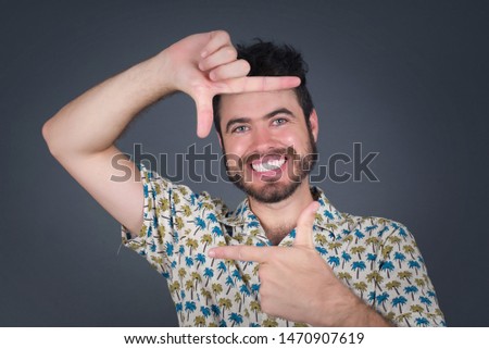 Portrait of young blond positive male with cheerful expression, dressed in casual shirt, has good mood, gestures finger frame actively at camera.
