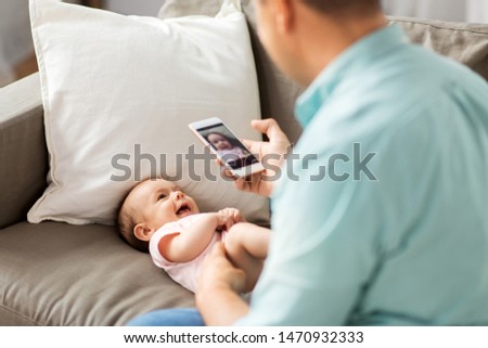 family, technology and fatherhood concept - middle aged father with smartphone taking picture of his little baby daughter lying on sofa at home