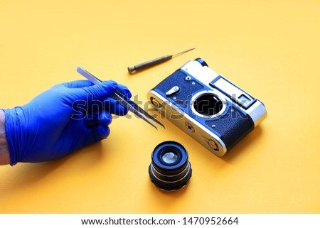 Vintage camera lens and tools, tweezers and a screwdriver with yellow paper background, camera repair concept. Old type.