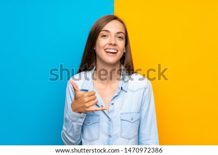 Young woman over colorful background making phone gesture