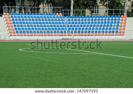  Grass field and plastic seats at stadium, open door sports arena.