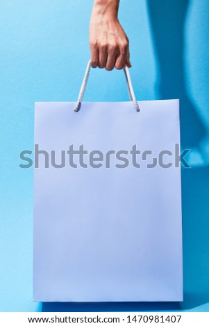 cropped view of woman holding purple shopping bag on blue background 