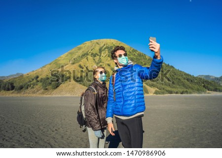 Young man and woman tourists make a selfie in the Bromo Tengger Semeru National Park on the Java Island, Indonesia. They enjoy magnificent view on the Bromo or Gunung Bromo on Indonesian, Semeru and