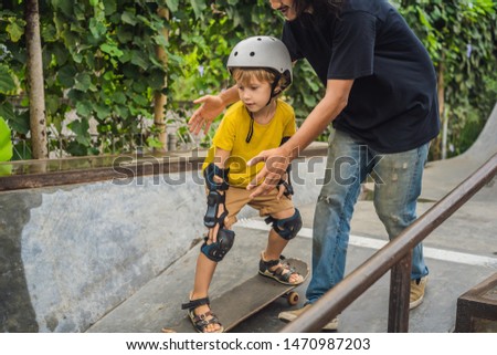 Athletic boy learns to skateboard with a trainer in a skate park. Children education, sports
