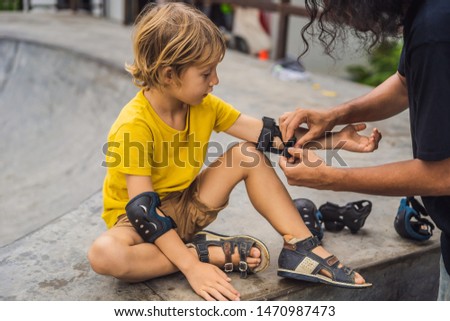 Trainer helps the boy to wear knee pads and armbands before training skate board