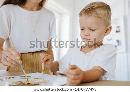 Mom is painting picture with her son on a sheet of paper with acrylic paints. Close up, cropped
