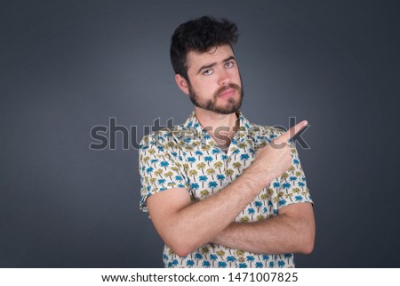 Excited surprised fashionable boy points happily aside on copy space of gray background for your fashion clothing advertising information or promotional text.