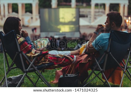 couple sitting in camp-chairs in city park looking movie outdoors at open air cinema lifestyle