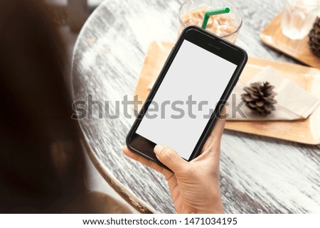 Mockup image of hands holding and using mobile phone with blank screen on wooden table in cafe.