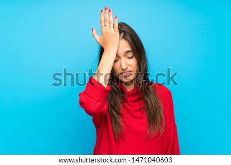 Young woman with red sweater over isolated blue background having doubts with confuse face expression