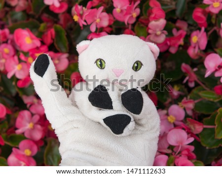 White funny toy kitten on the pink flowers background.  Conceptual photography.