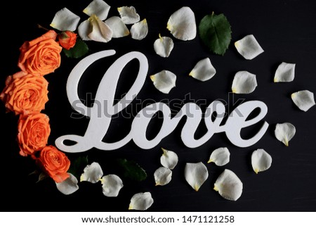 Word love on a black background with roses and petals