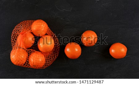 Oranges in net, some scattered on black stone like board, flat lay photo