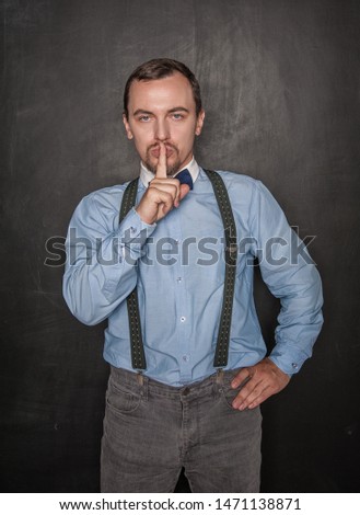 Handsome man with finger on lips on blackboard background